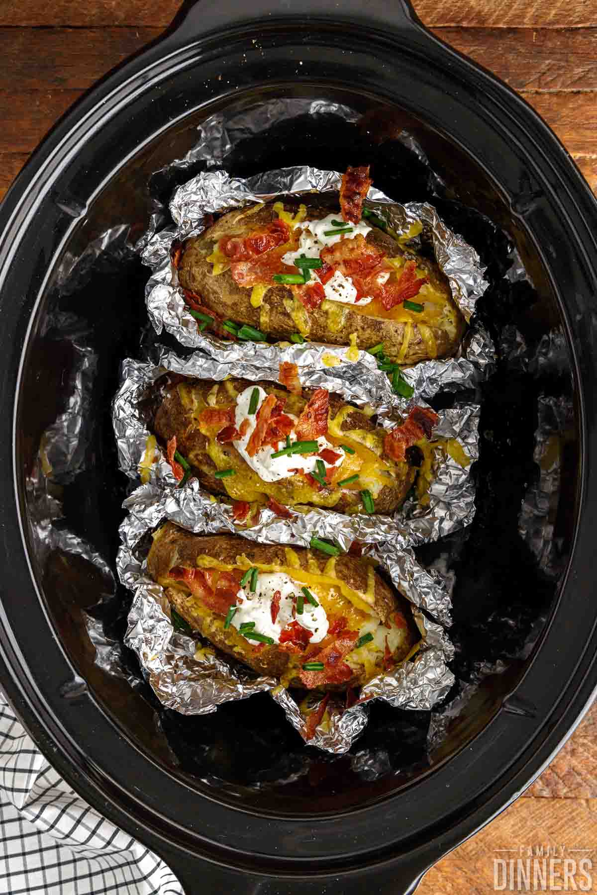 3 baked potatoes with toppings in a crockpot crock.