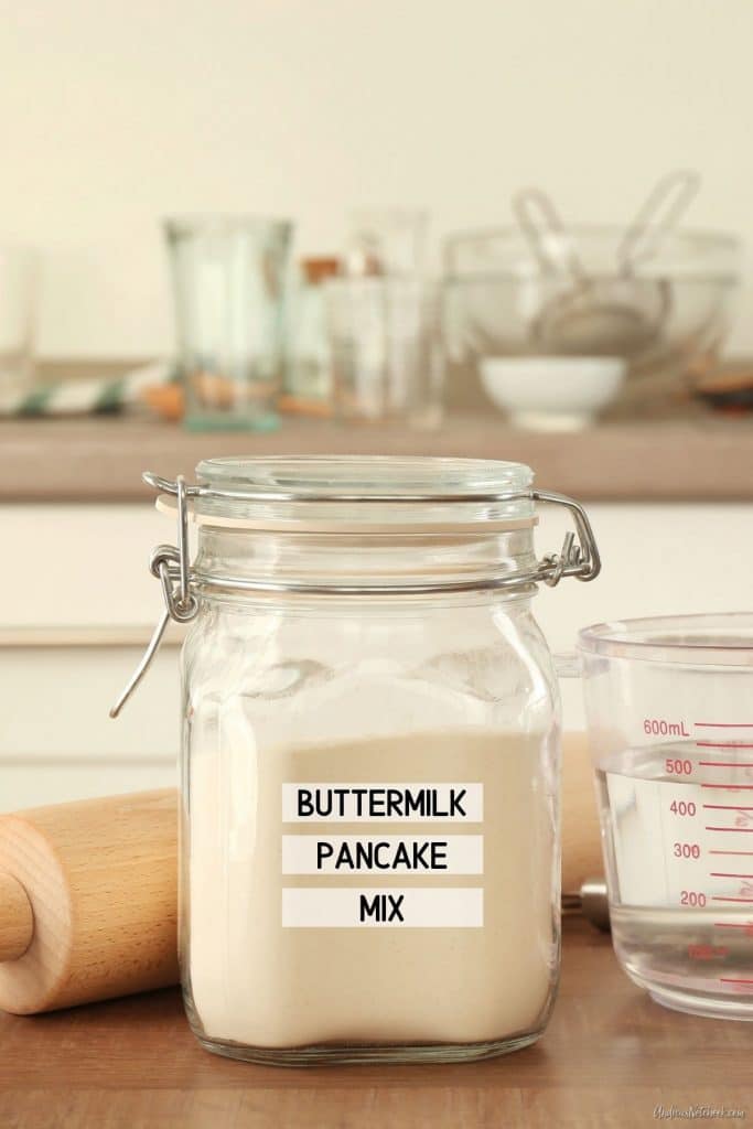 clear glass canning jar on counter in front of rolling pin and measuring cup. Jar is full of pancake mix. Label on jar says buttermilk pancake mix