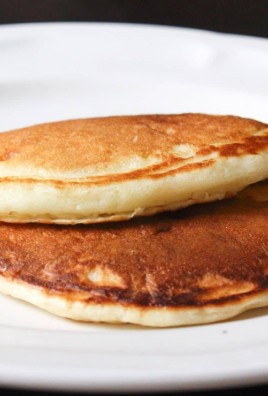 2 golden pancakes stacked together on a white plate with a black background