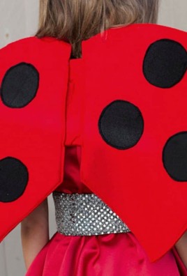 back view of kid wearing red ladybug wings with black polkadots. Wood fence in background.