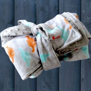 rolled up fuzzy baby blanket sewing pattern. Gray fabric with orange and aqua dino on a navy blue background