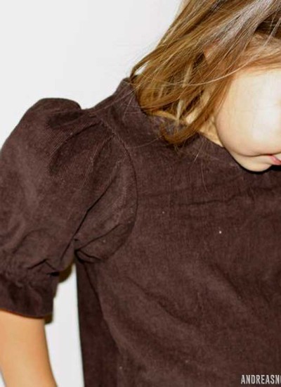 little girl with brown hair and golden skin wearing brown corduroy top with puffed sleeves