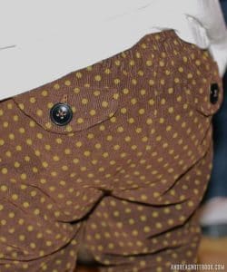 backside of small child with brown pants with little green dots and two pocket flaps with buttons
