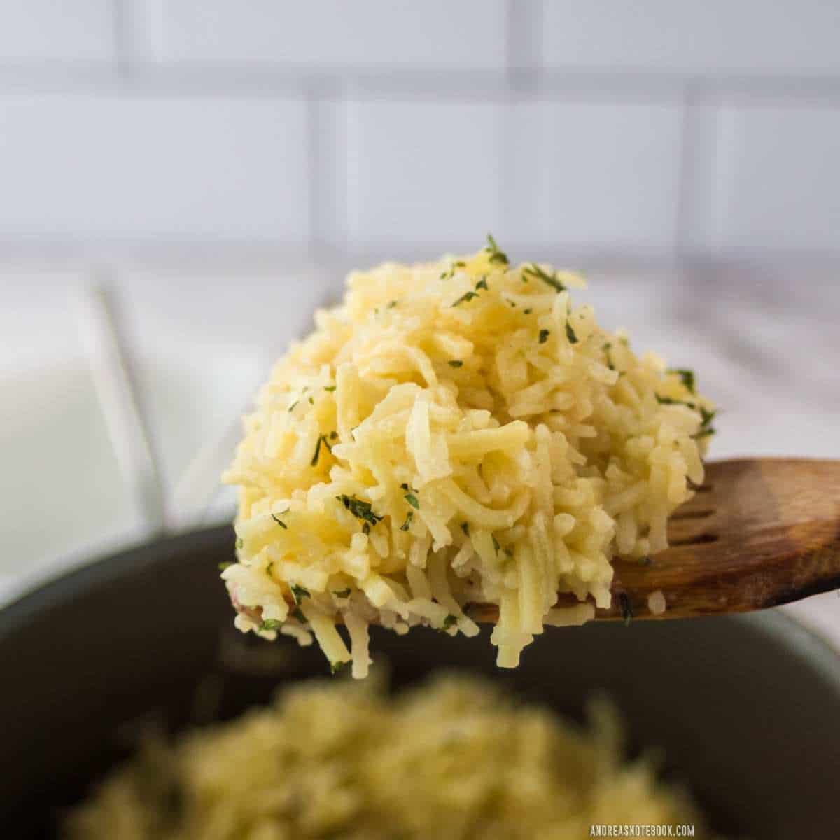 wooden spoon full of yellow rice-a-roni copycat rice with blurred black pot with rice in background