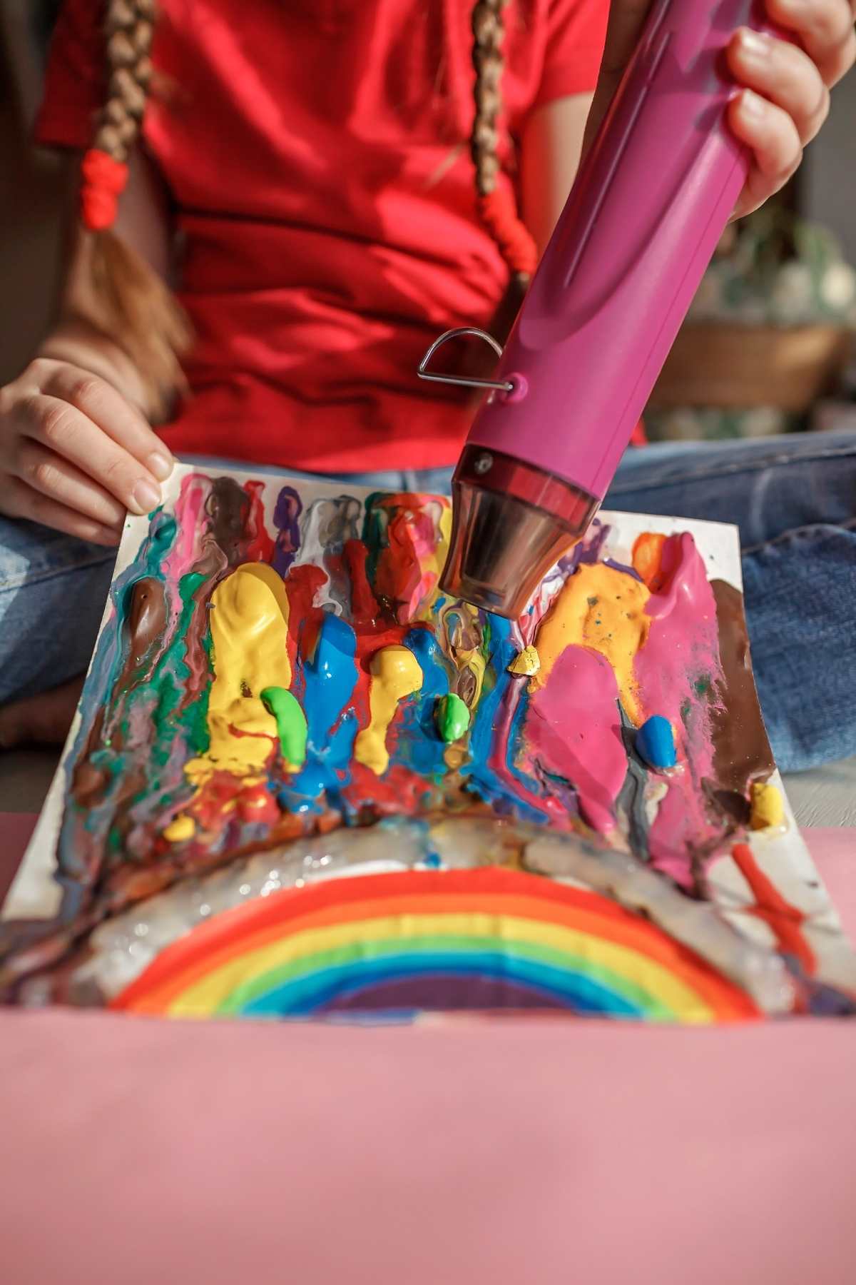 Girl holding hot air dryer melting crayon on paper.