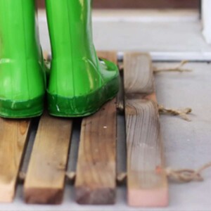 Green rubber boots on a rustic DIY wood plank dormat.