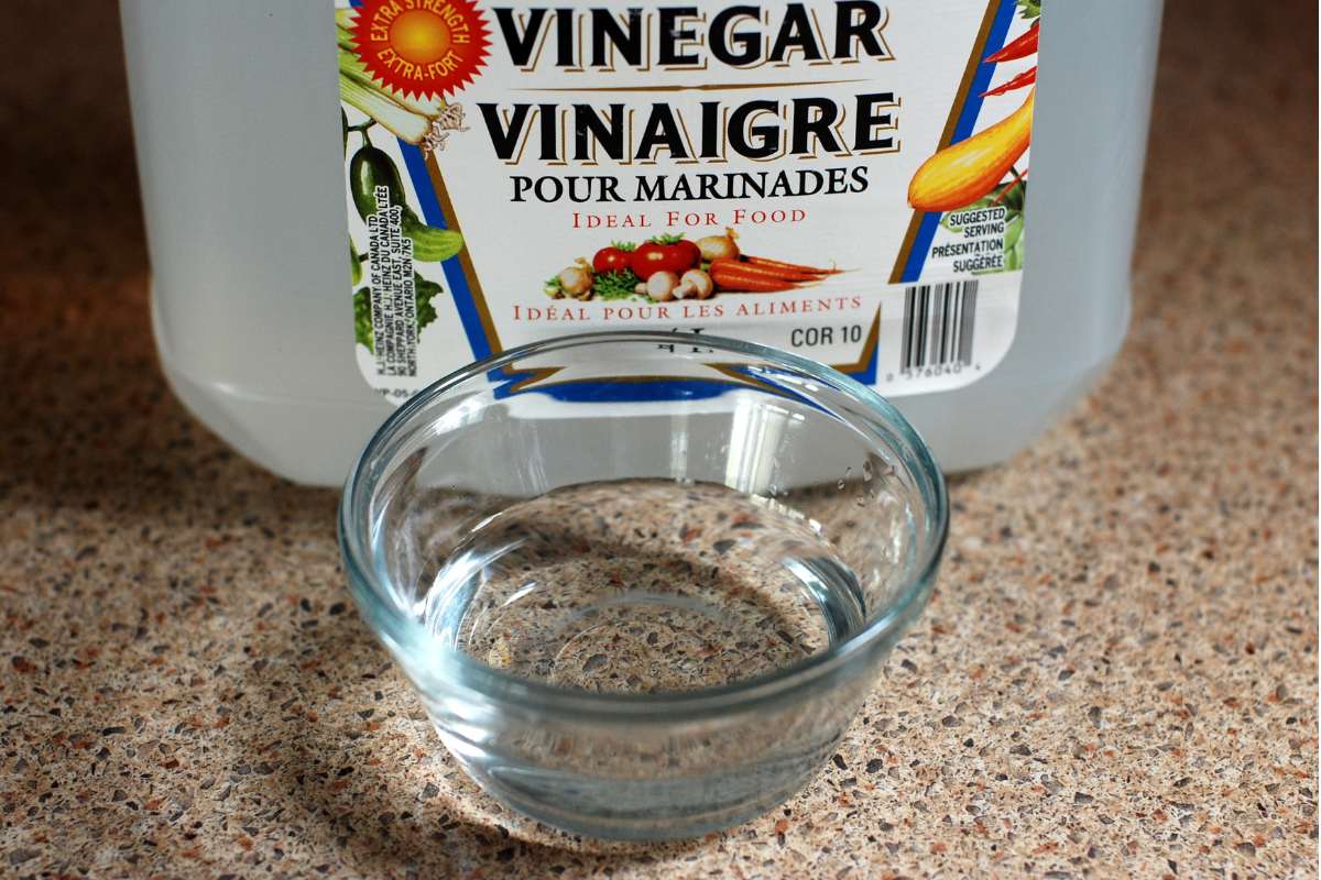 Plastic jug of white wine vinegar with a small glass bowl full of vinegar in front.