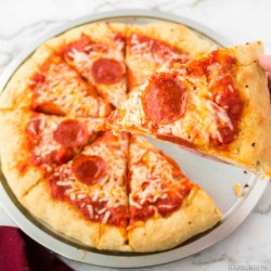 round pizza on a silver pizza pan with pizza sauce, cheese and pepperoni