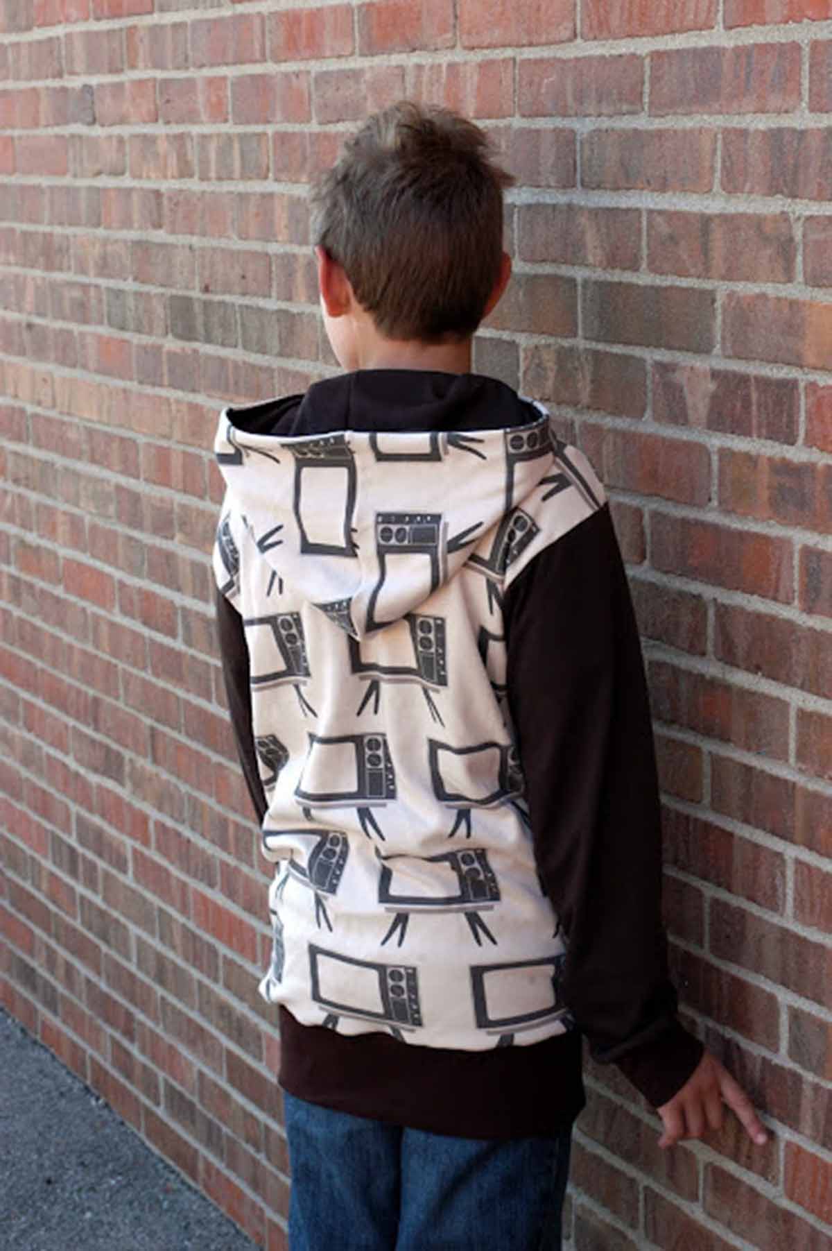 Boy in hoodie facing brick wall with hoodie off his head.