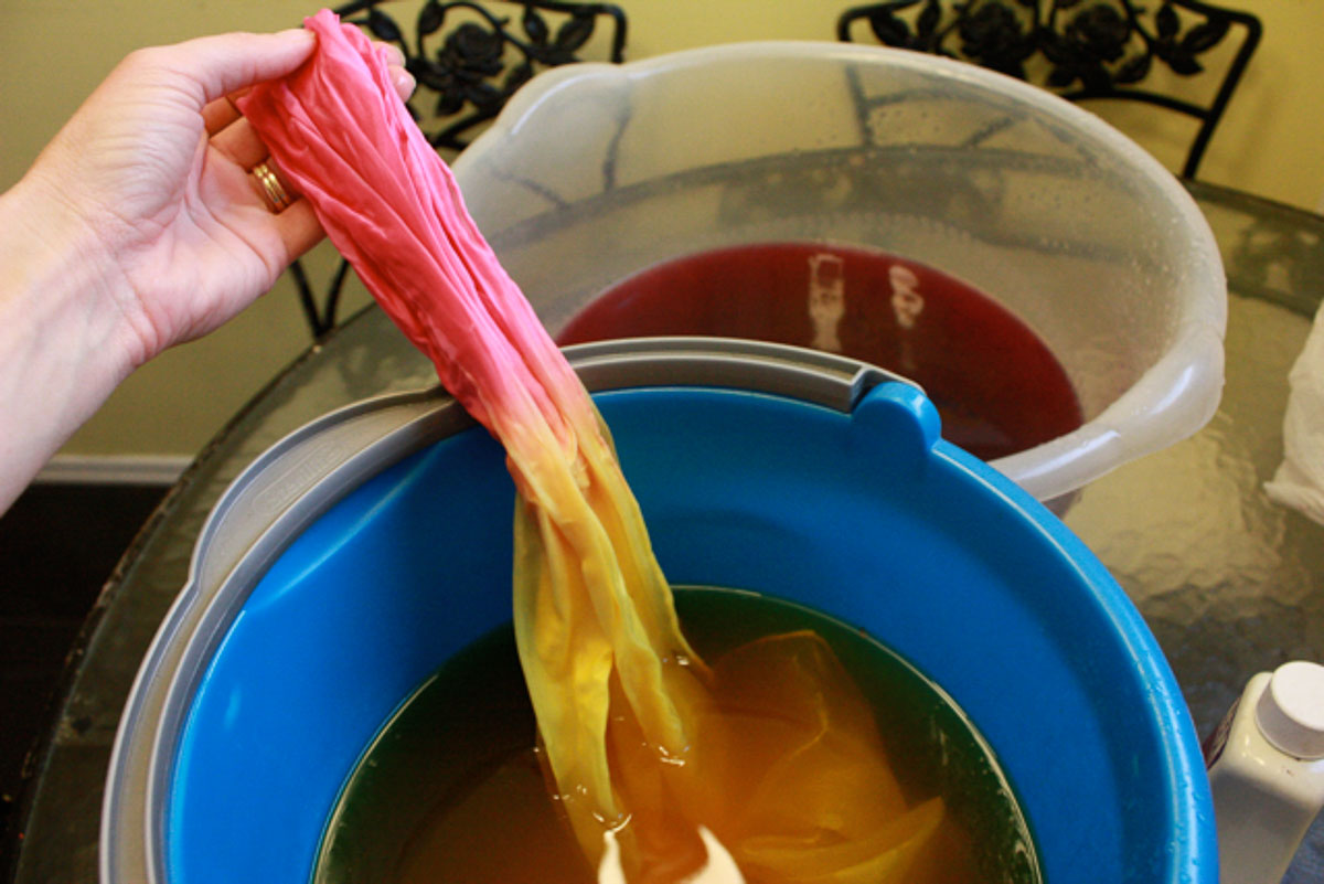 Silk scarf dipped in yellow dye in bucket.