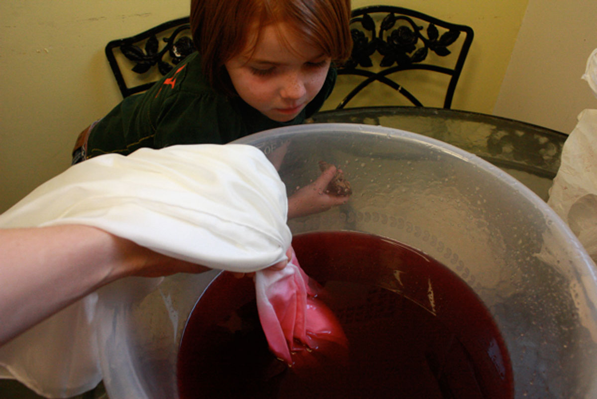 Silk scarf being dipped into pink dye in bowl.