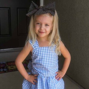 Little girl with big black bow on head and blue checkered dress.