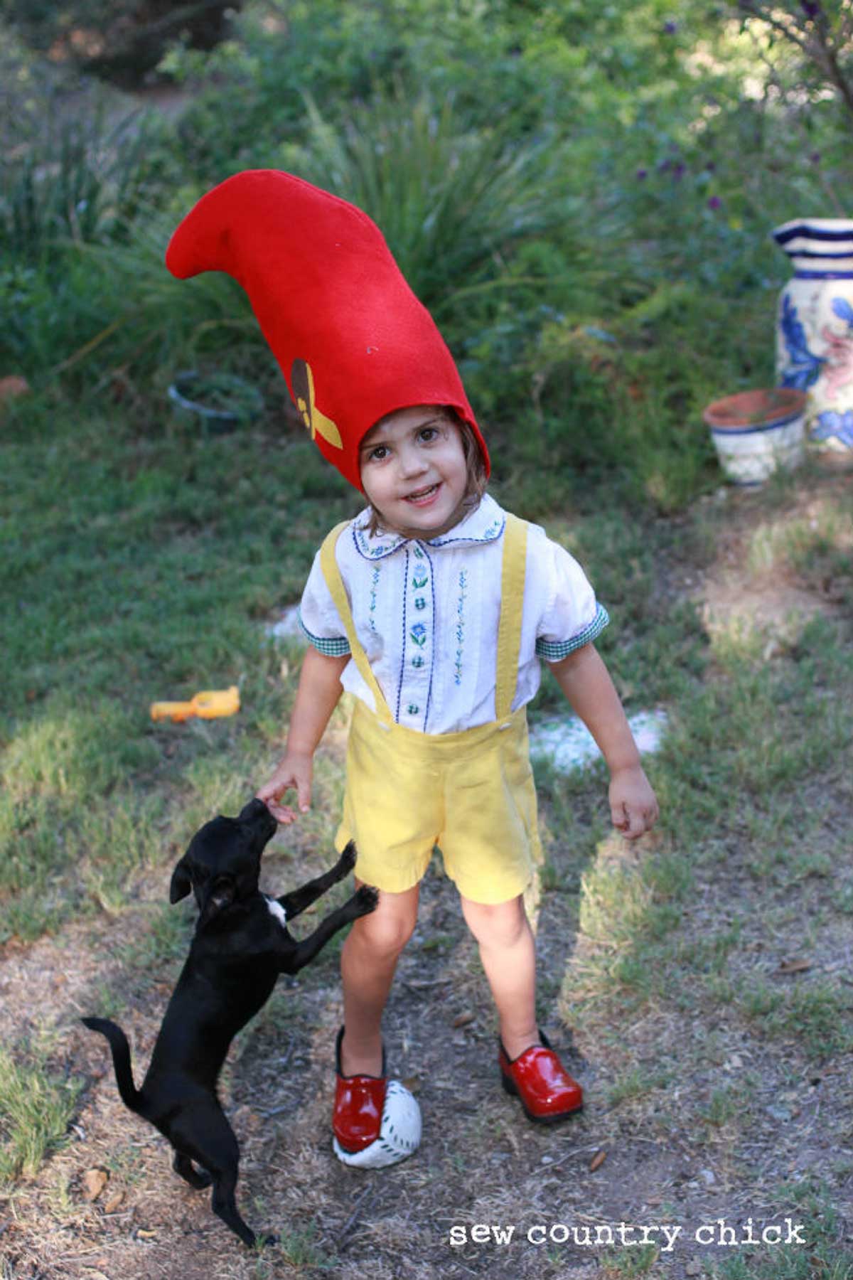 Little girl in a DIY garden gnome costume with a black little dog.