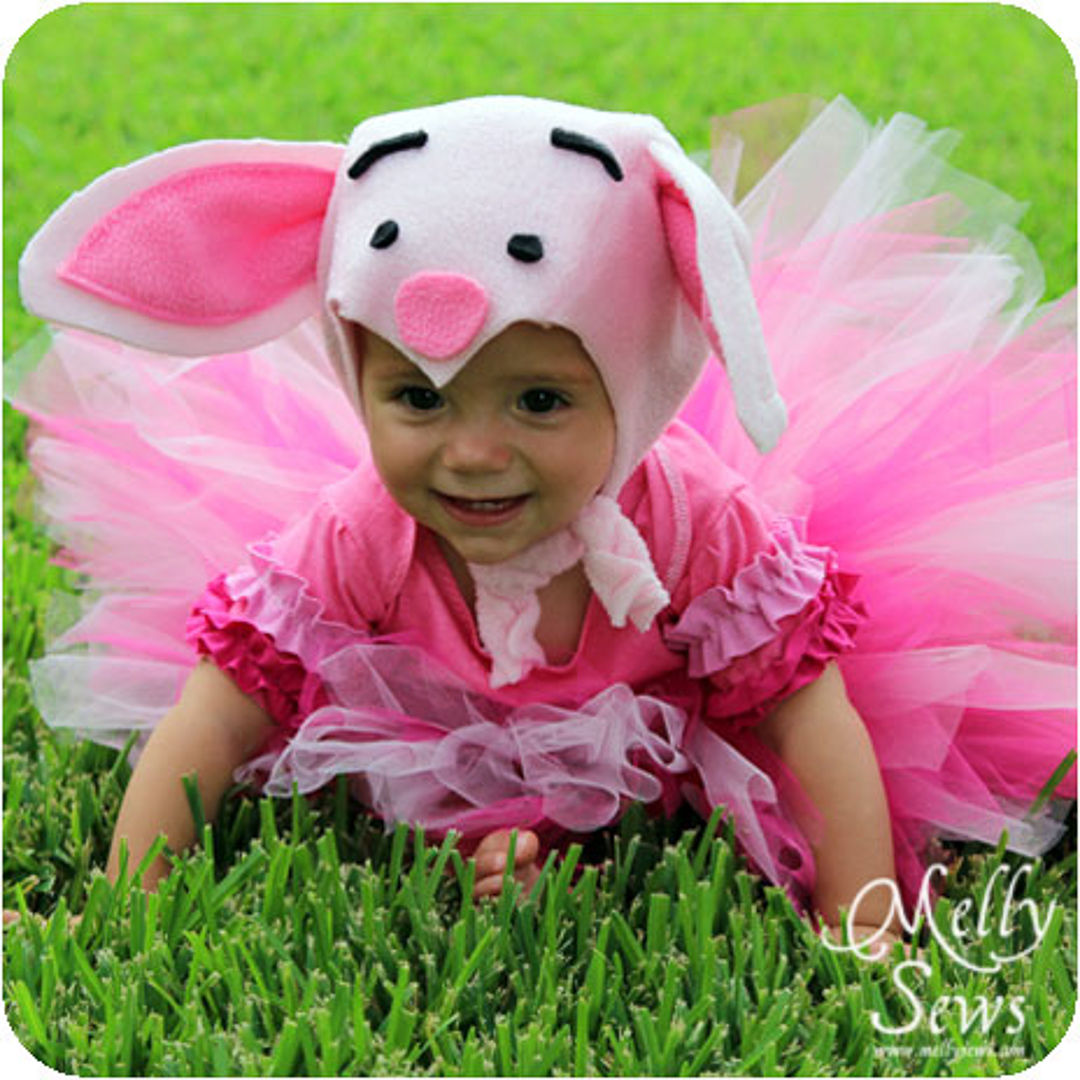 Little girl sitting in grass in piglet costume.