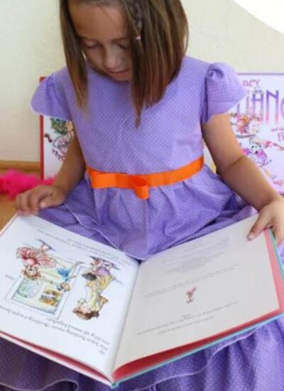 GIrl in purple DIY fancy nancy costume reading the Fancy Nancy book.