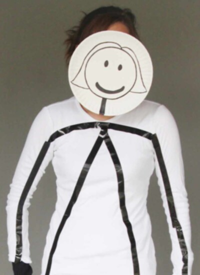 Person in an all white outfit with black tape on top making a stick figure and a cartoon head in front of their face.