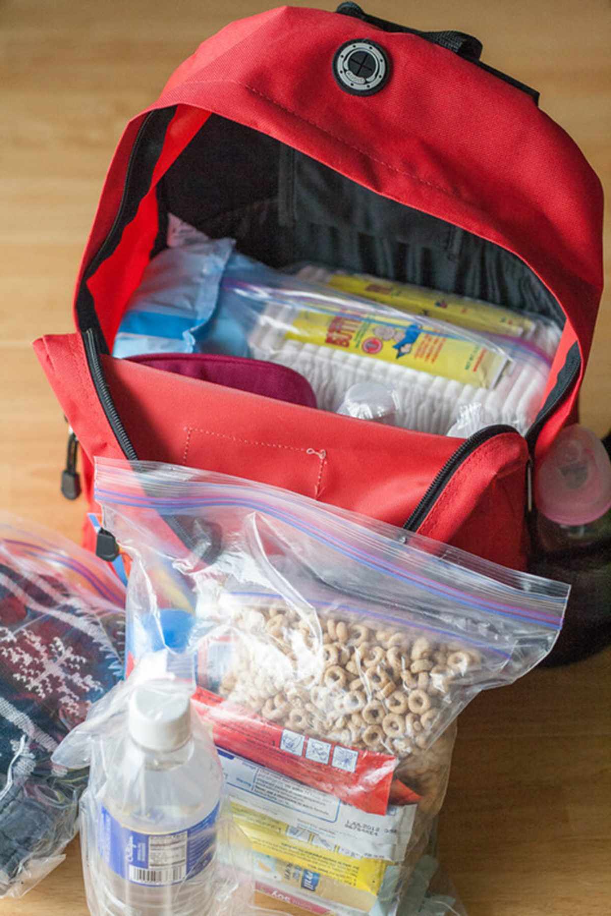 Red backpack open and full of baby supplies including cheerios.