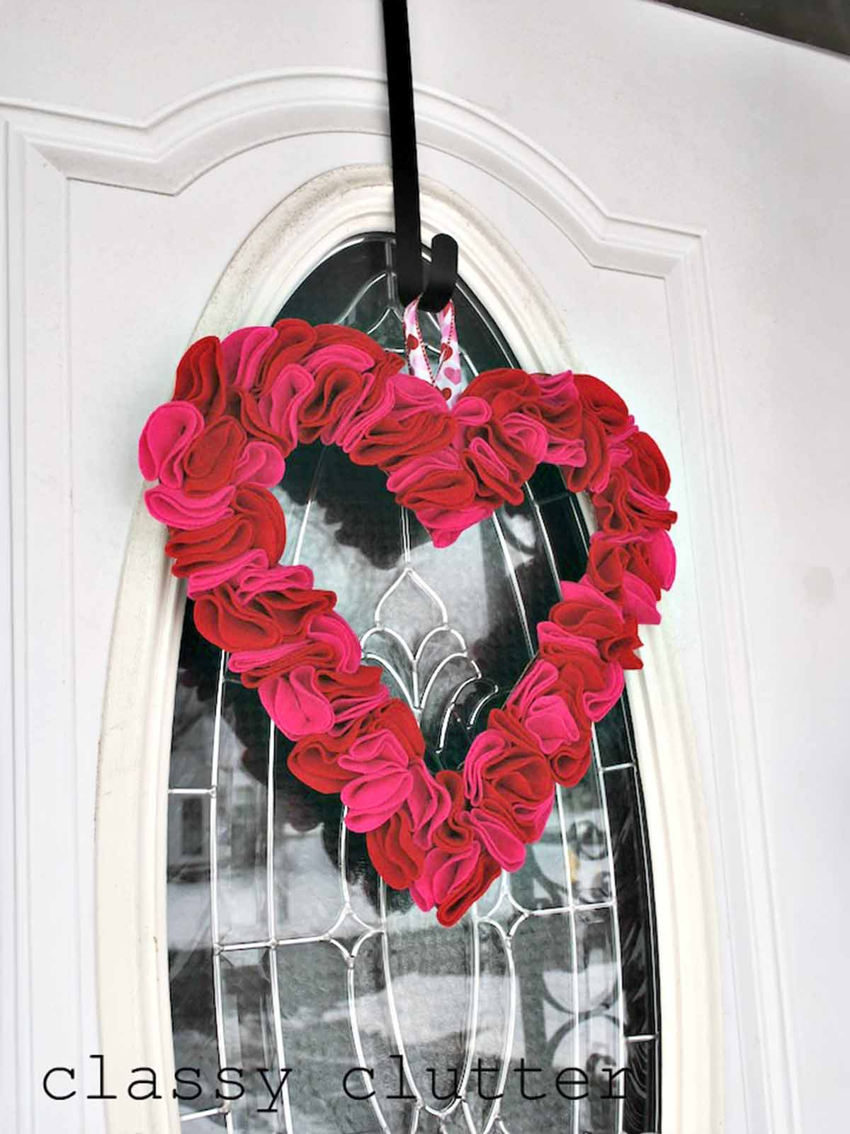 Red and pink heart shaped DIY Valentine's Day wreath with felt hearts on a white door.