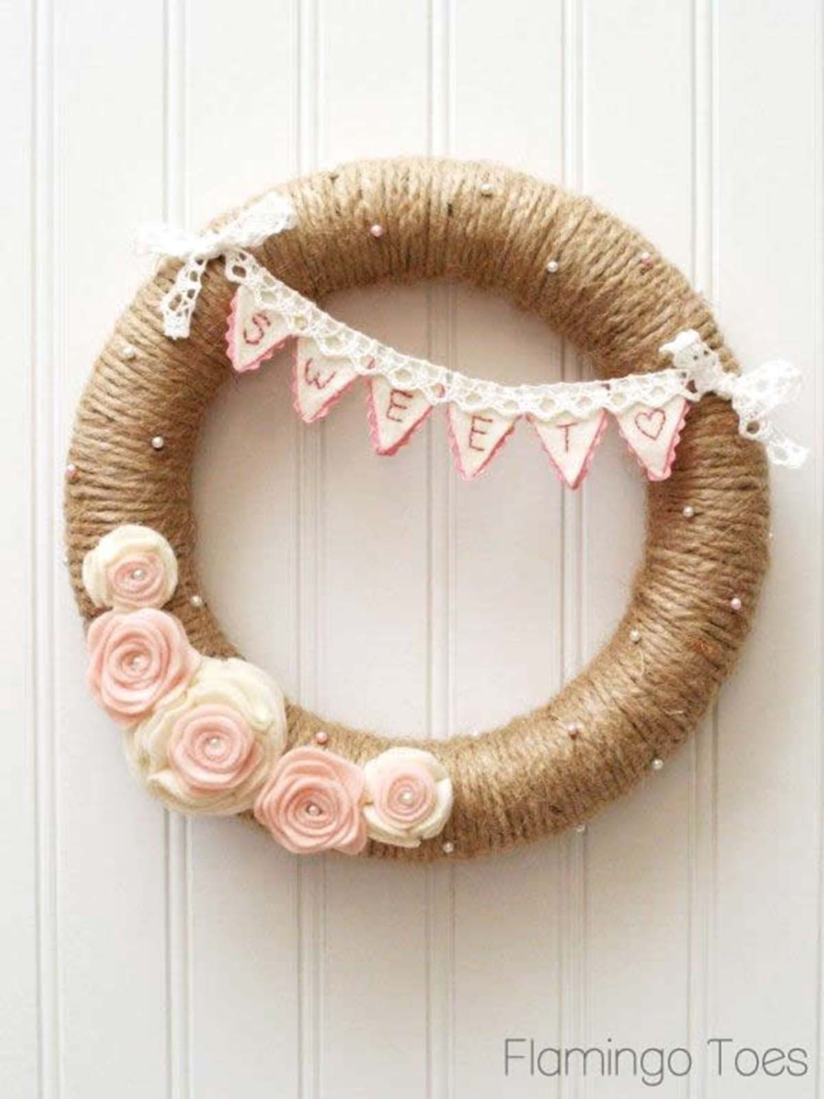 Round burlap Valentine's Day wreath with pink and white felt rosettes on the bottom and a felt bunting on top.