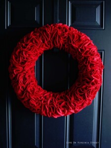 Round red DIY felt ruffle wreath on a dark navy blue door.