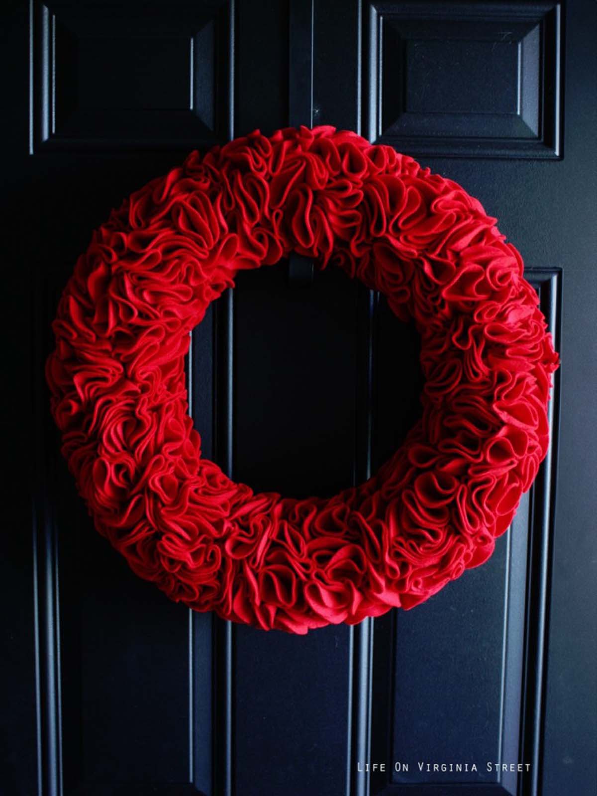 Round red DIY felt ruffle wreath on a dark navy blue door for Valentine's Day or Christmas.
