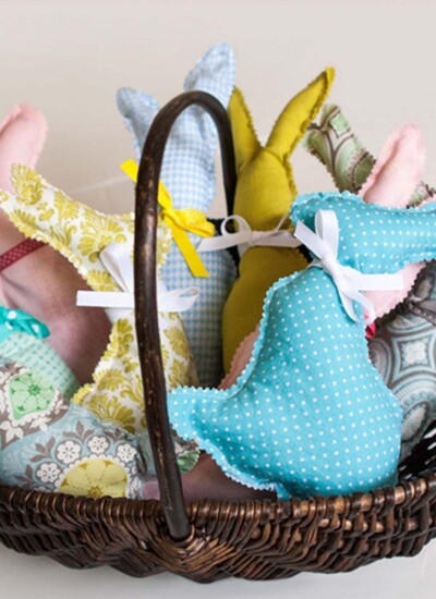 Basket with a handle full of simple stuffed bunny pillows with ribbon bows on their necks.