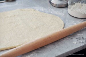 Yeast dinner roll dough rolled out on a lightly floured surface next to a wooden rolling pin.