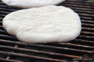 Flattened pizza dough round on the grill.
