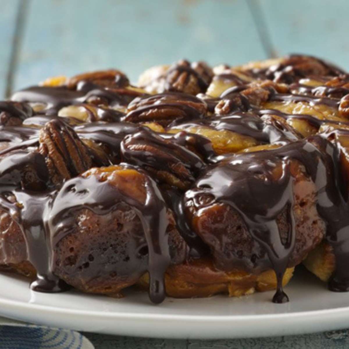 Slow cooker turtle monkey bread with pecans and a chocolate drizzle on a plate.
