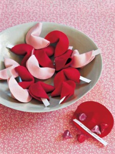 Gray bowl full of red and pink felt fortune cookies with fortunes sticking out.