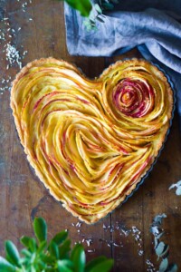 Heart shaped tart pan with thinly sliced apples inside to make a rose shape.