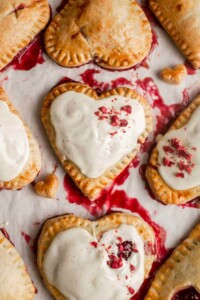 Golden crusted heart shaped hand pies with white frosting on top and sprinkles.