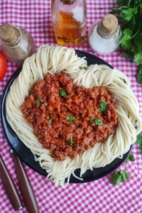Plate of spaghetti twisted into a heart shape with hear shaped pile of sauce in the middle.