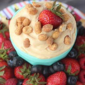 Peanut butter cheesecake dessert fruit dip in a bowl topped with peanuts and a strawberry.