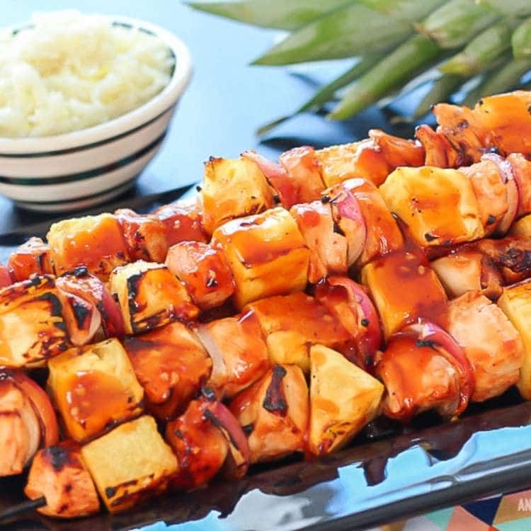 black rectangular plate with a stack of kabab skewers with pineapple, pineapple and onion with a glaze on top