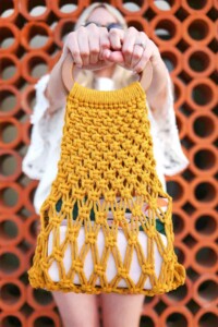 Easy DIY macrame bag made from yellow material and hoop closure being held by a woman.