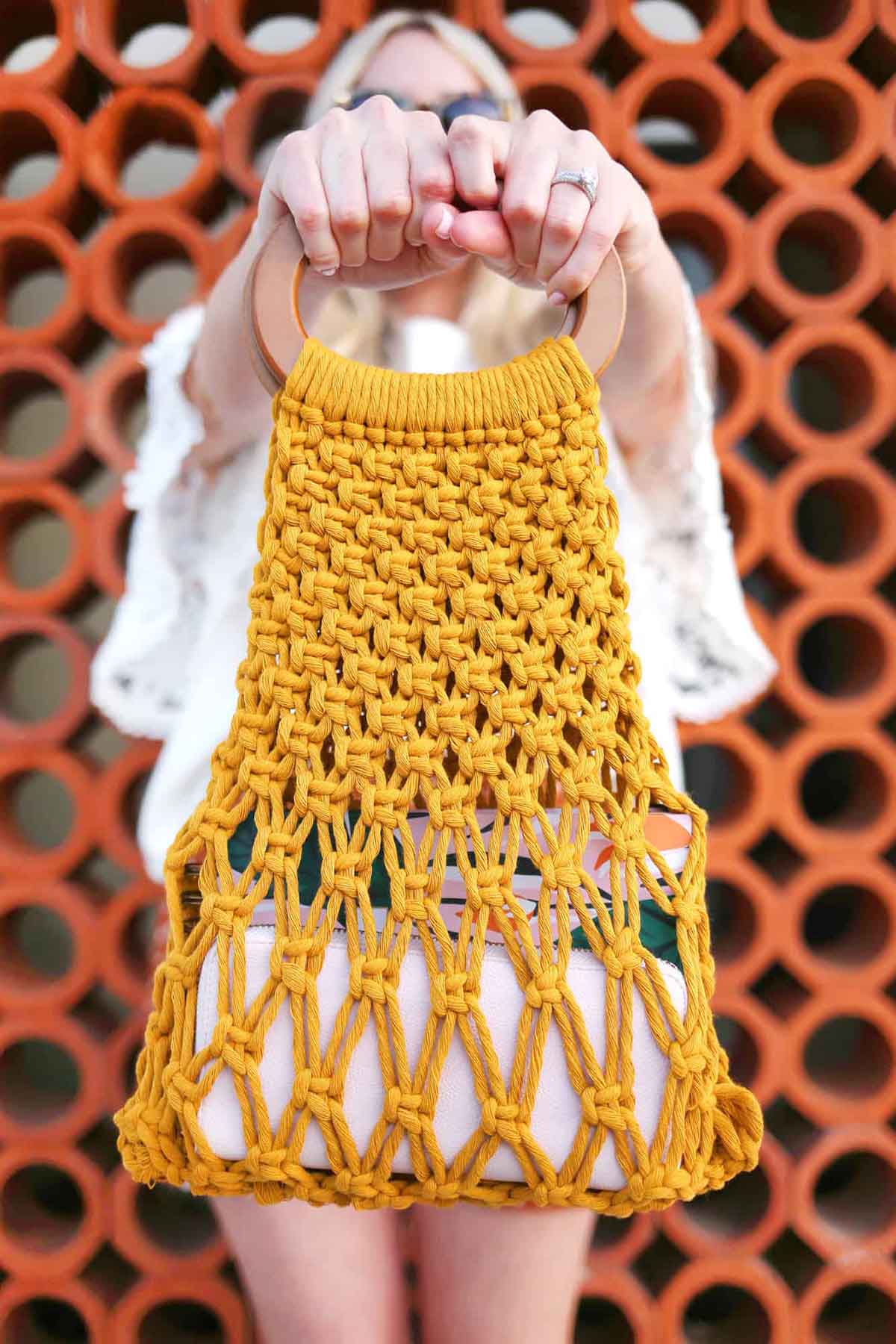 Easy DIY macrame bag made from yellow material and hoop closure being held by a woman.