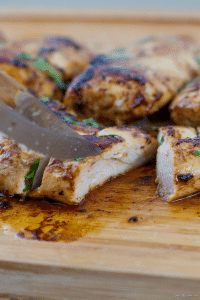 juicy cooked chicken breasts on a cutting board with cilantro on top
