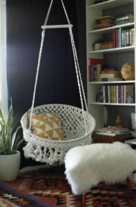 Hanging DIY macrame chair tutorial by classy clutter hanging in a room with a pillow inside.