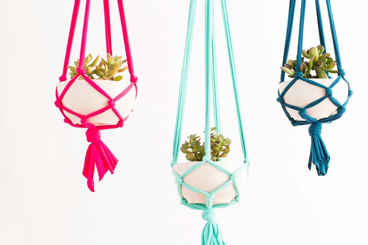 3 bold colored t-shirt yarn macrame plant hangers holding white planters.