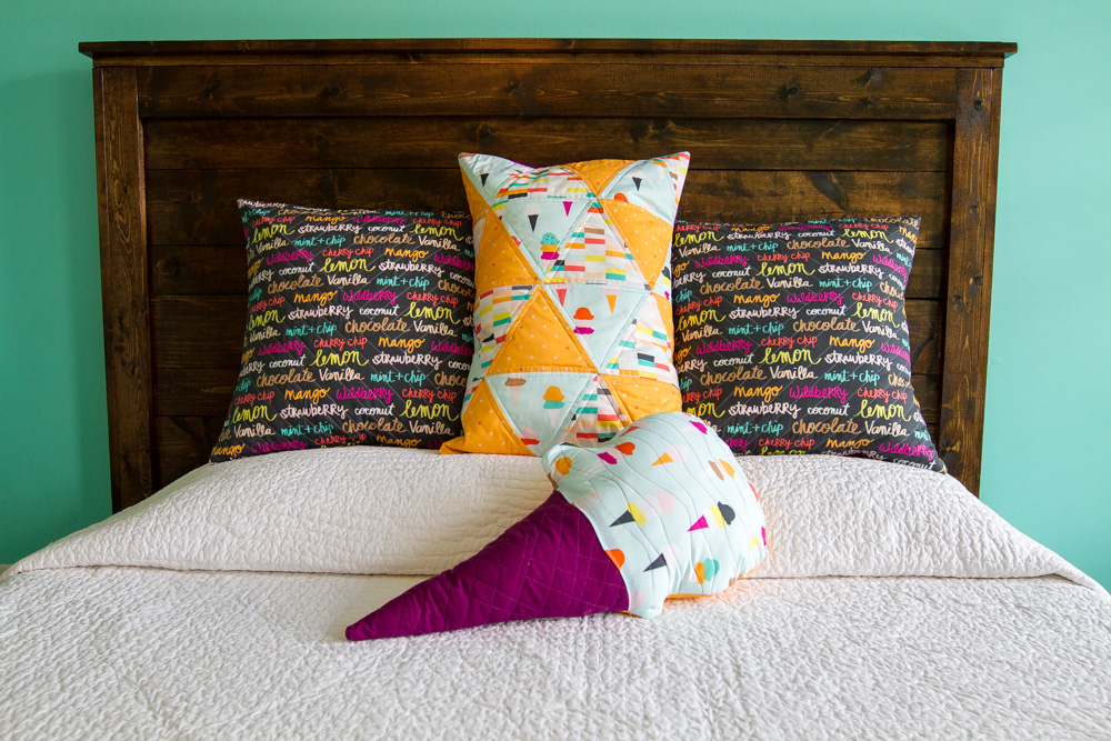 two square quilted pillows and one rectangular quilted pillow and one ice cream cone shaped pillow on bed with white cover 