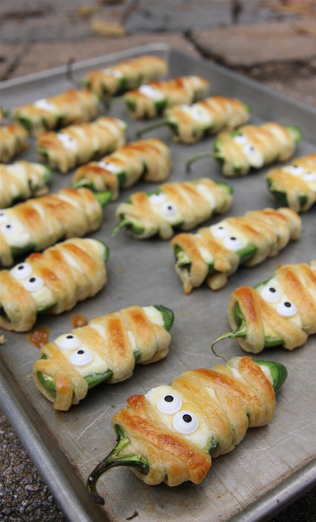 Mummy jalapeno poppers on a tray with dough baked around jalapeno pepper as a mummy wrap.