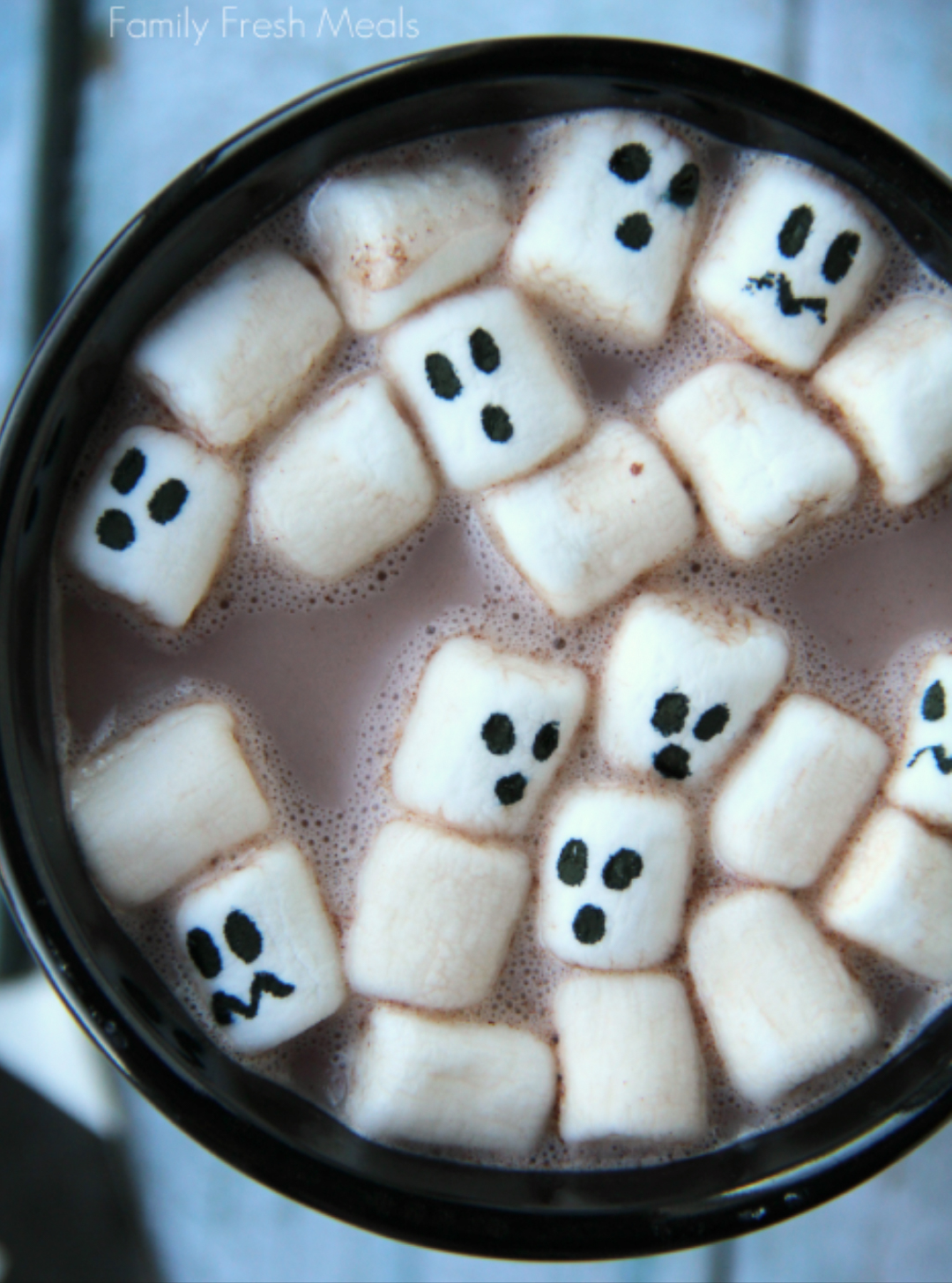 Marshmallows with ghost faces in hot cocoa as a scary Halloween drink.