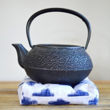 black cast iron teapot on white and blue tea trivet