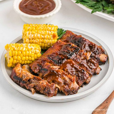 Plate full of bbq baby back ribs and corn on the cob.
