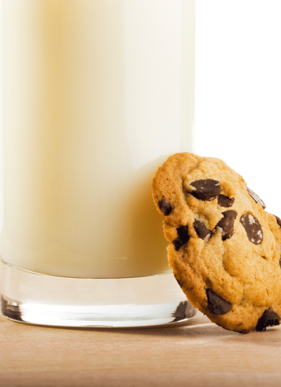 one cookie leaning against a glass of milk