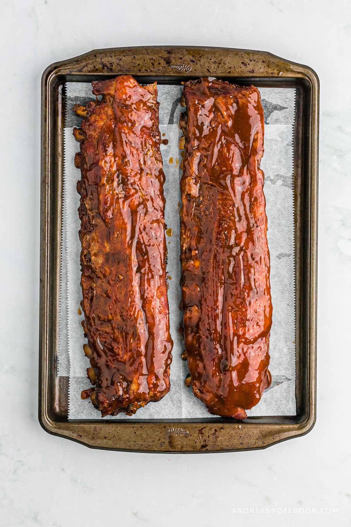 Full rack of baby back ribs on a baking sheet.