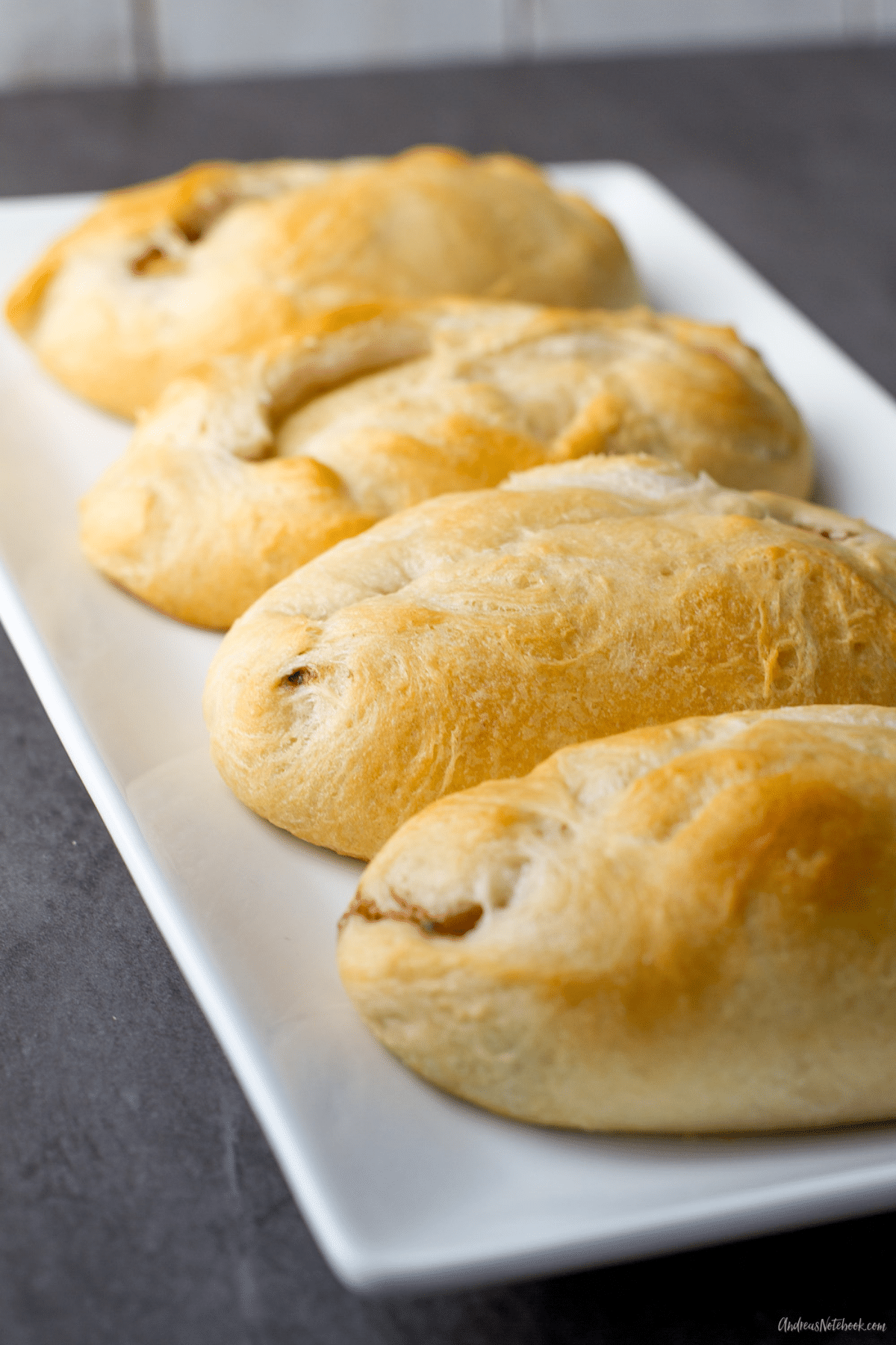 4 large croissant looking rolls on a rectangular white plate.