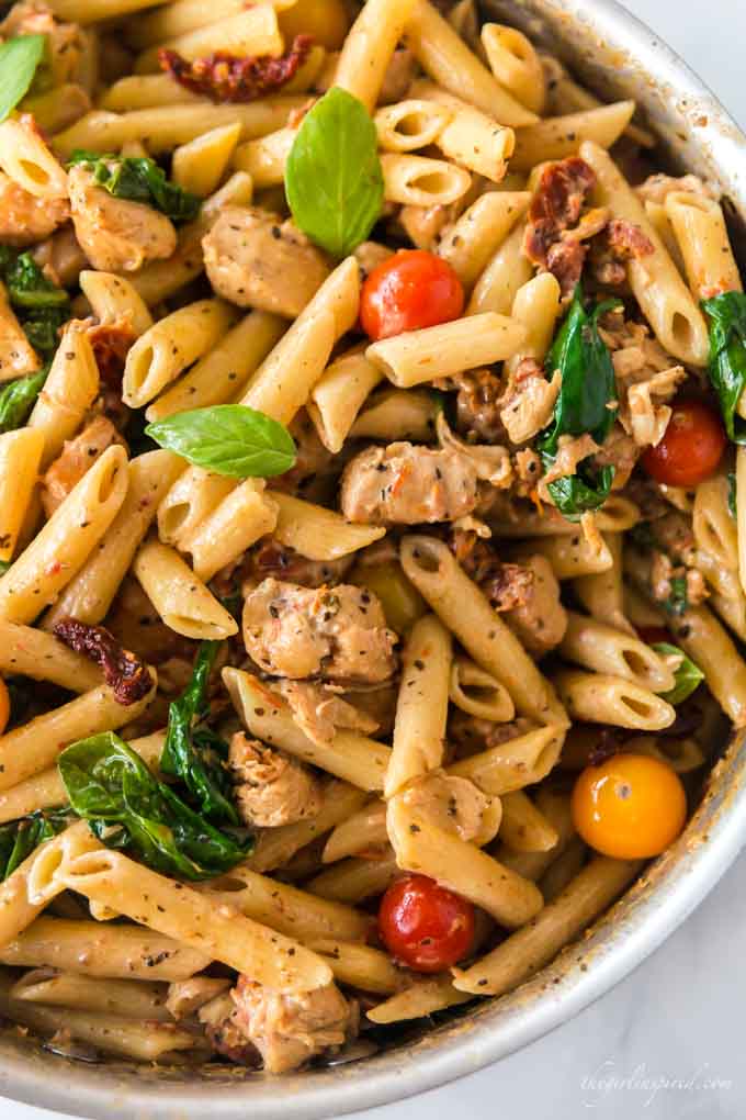 Pot full of diced chicken, penne pasta, spinach and small tomatoes in a cream sauce.