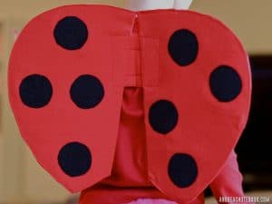 back of girl's torso in red shirt wearing red ladybug costume wings with black polkadots